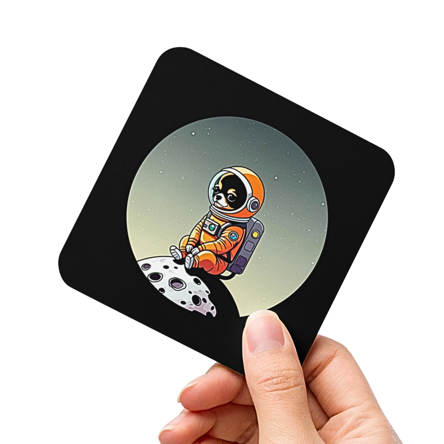 Photo of a hand holding a square black coaster printed with a cute illustration of a Chihuahua dog wearing an astronaut suit sitting on a small moon.