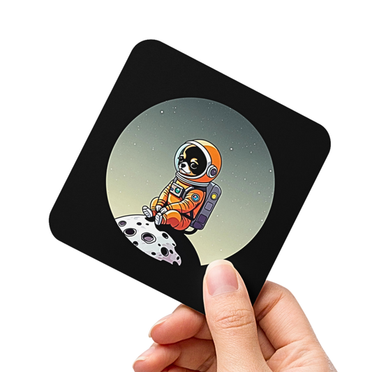 Photo of a hand holding a square black coaster printed with a cute illustration of a Chihuahua dog wearing an astronaut suit sitting on a small moon.