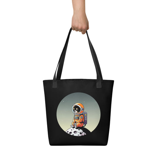 Picture of a hand holding a black color tote bag printed with an adorable illustration of a Chihuahua Dog, in an astronaut suit sitting in a small moon.